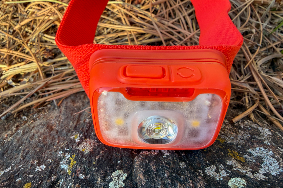 Front view of a red BioLite headlamp resting on a rock, showing the wide frosted lens and top control buttons.
