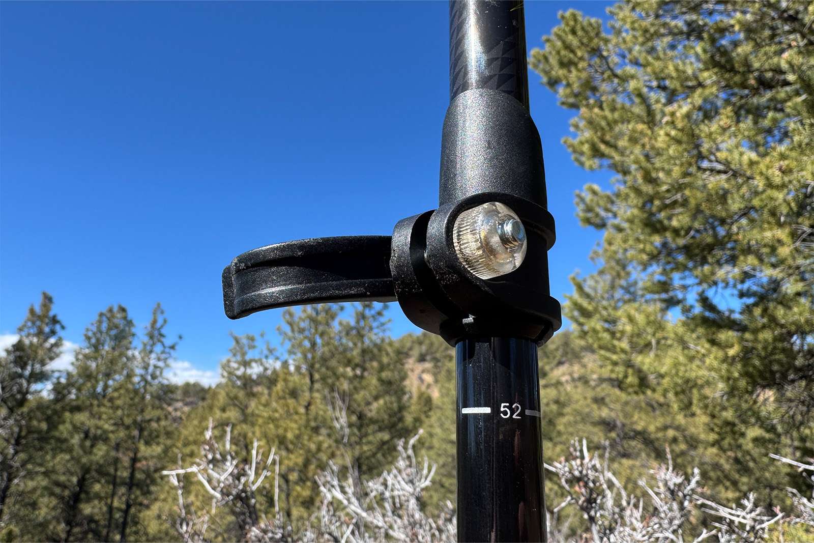 A close up of an open flick lock and tensioner on the Cascade poles. There are pine trees and clear skies in the background.