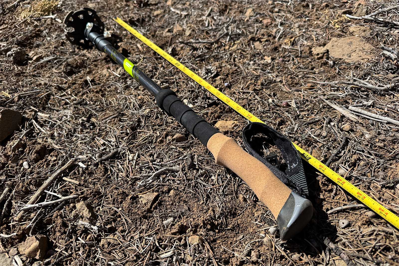 A cascade pole is laying on the ground collapsed with a measuring tape extended next to it.