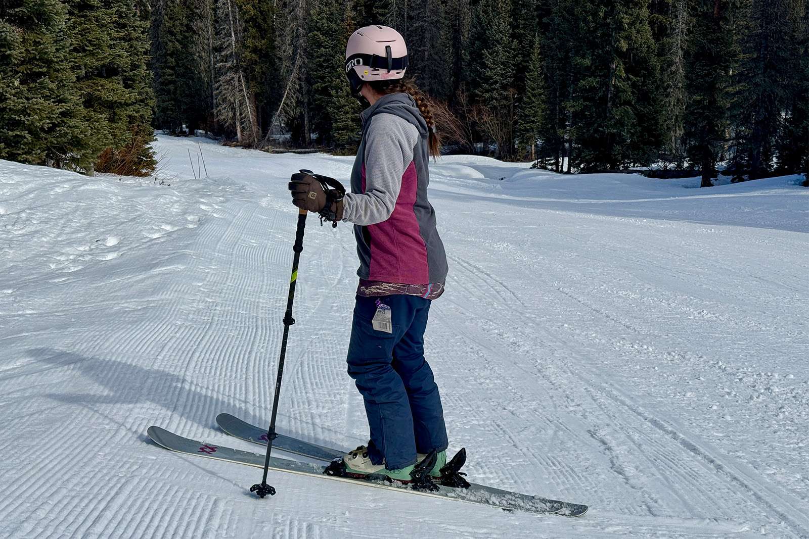 A skier is standing on a run holding the Cascade poles and looking down the hill.