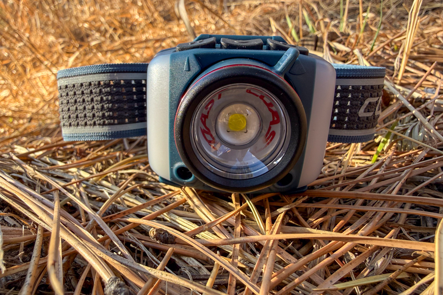 Close-up of the Coast FL95R Headlamp front lens and reflector, resting in dry pine needles.