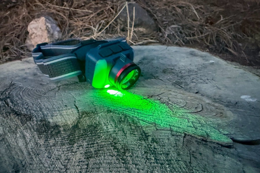 Coast FL95R headlamp on a log at dusk with the green LED mode on, casting a bright green beam across the wood.