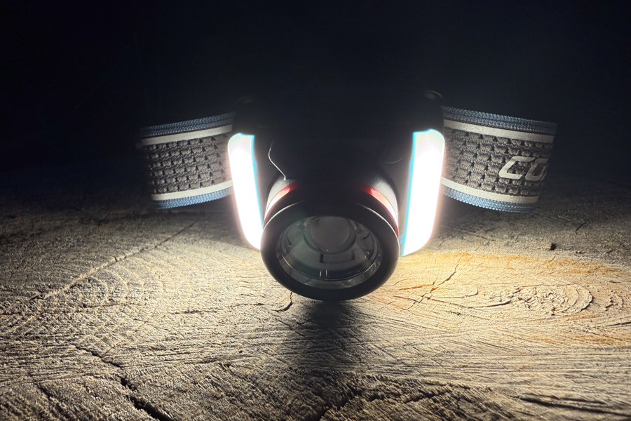 Front view of the Coast FL95R on a log at night with the side area lights glowing, illuminating the wood surface.