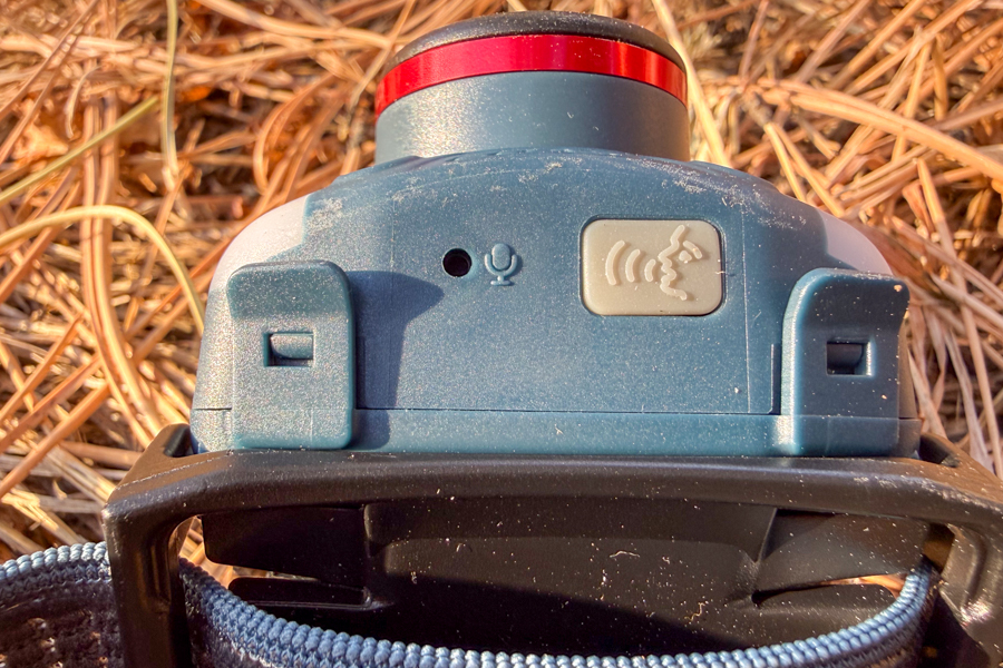 Close-up of the Coast FL95R showing the voice-activation icon and microphone opening on the underside of the headlamp body.