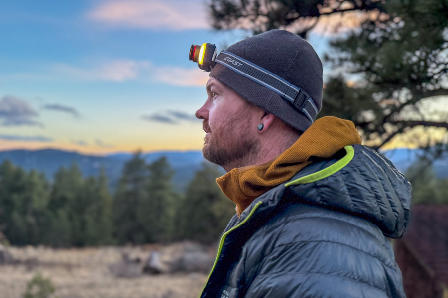 Side profile of a person wearing the Coast FL95R on a beanie at dusk with mountains and trees in the background.