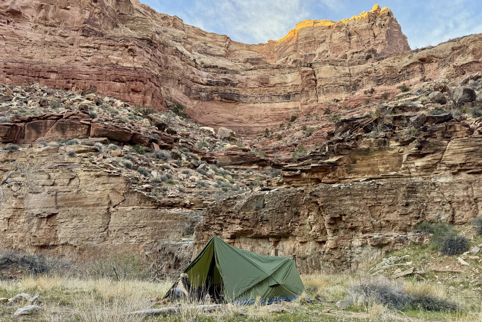 The Trekker tent is set up in some grass at the bottom of a canyon. There are red cliff walls rising behind it.