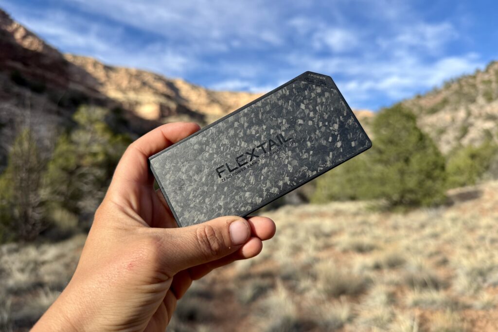 Close up of a hand holding the Flextail up to the camera. There is a pinion-juniper forest and canyon in the background.