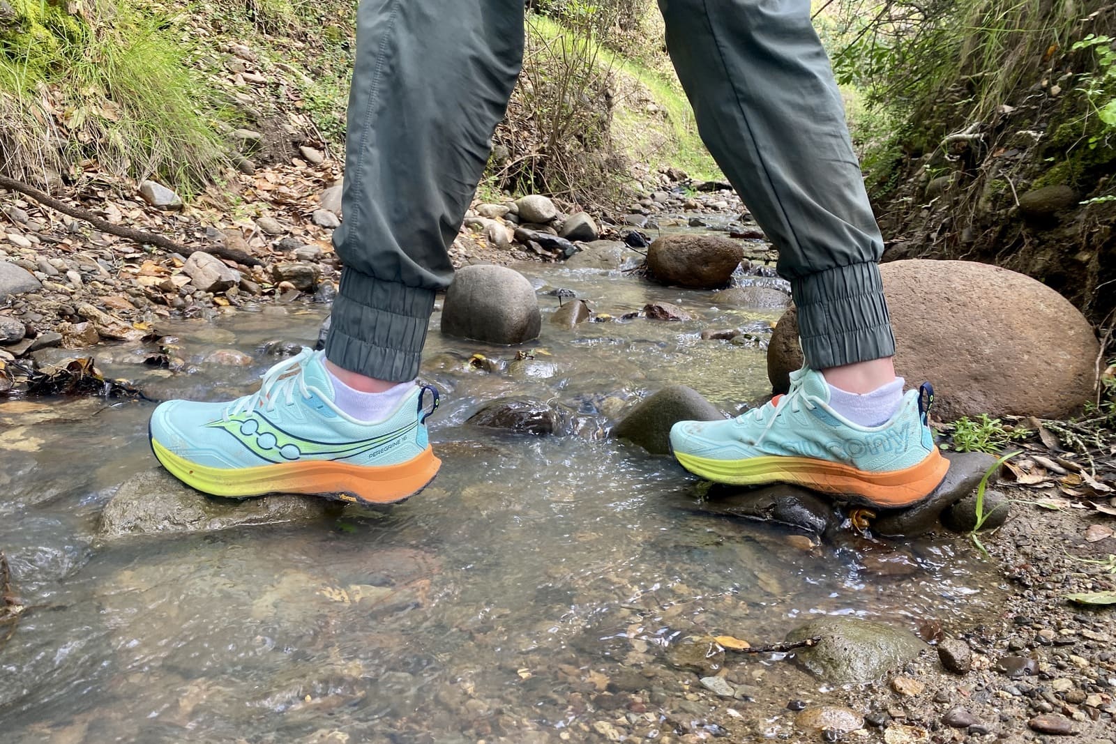 A woman crosses a creek in her trail shoes.