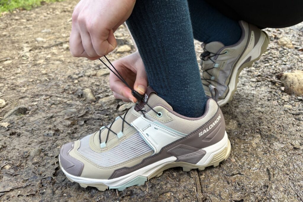 A woman cinches up her hiking shoe.