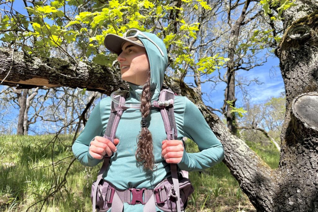 A woman stands on a trail showing the front of her hydration pack.