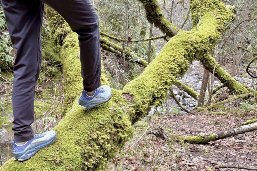 A woman walks across a mossy log.