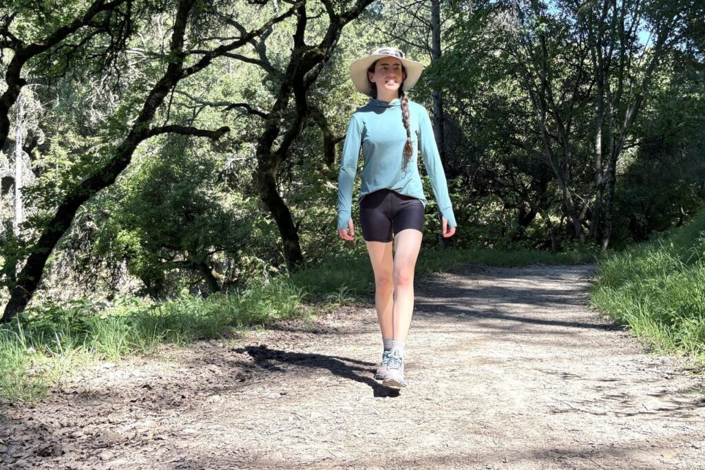 A woman walks along a forested trail.