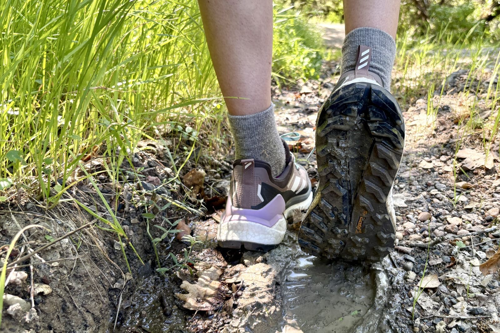 Closeup showing the tread of a pair of shoes as a woman hikes through mud.