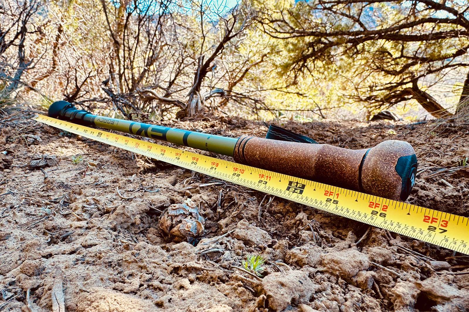 Close up of the packed down Legacy pole laying on a pine needle covered ground with a measuring tape extended next to it and pine trees in the background.