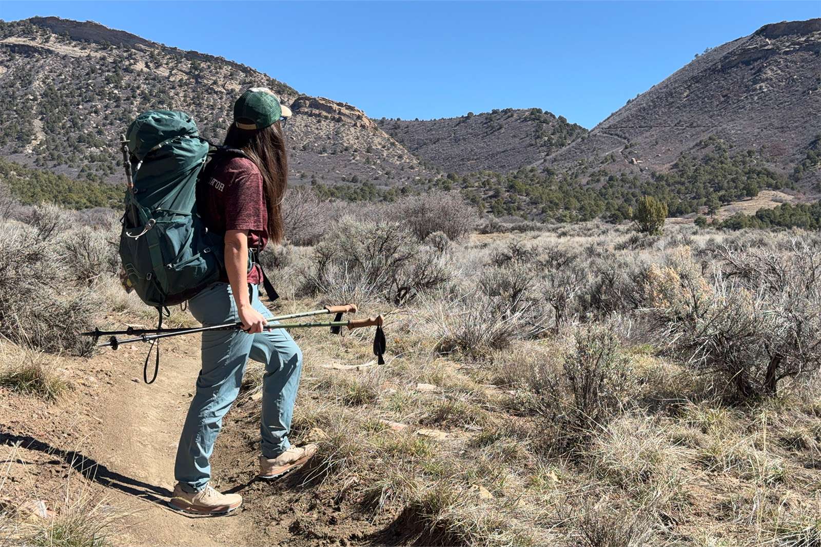 A person wearing a pack and holding the Legacy poles is stopped to look a view of some buttes across a grassy valley.