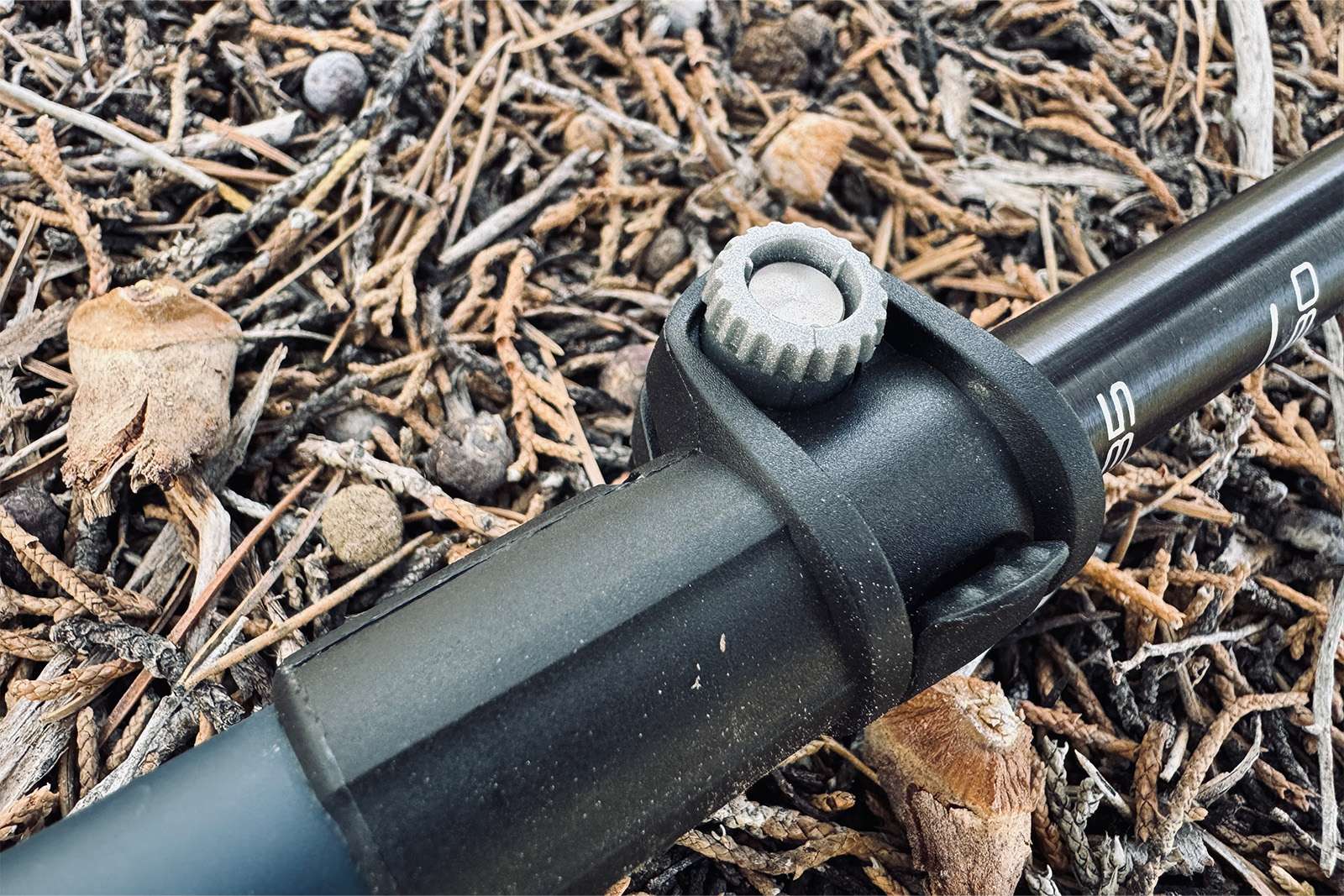 Close up of the tensioner on the flick lock of the Legacy pole. The pole is laying on a pine needle covered ground.