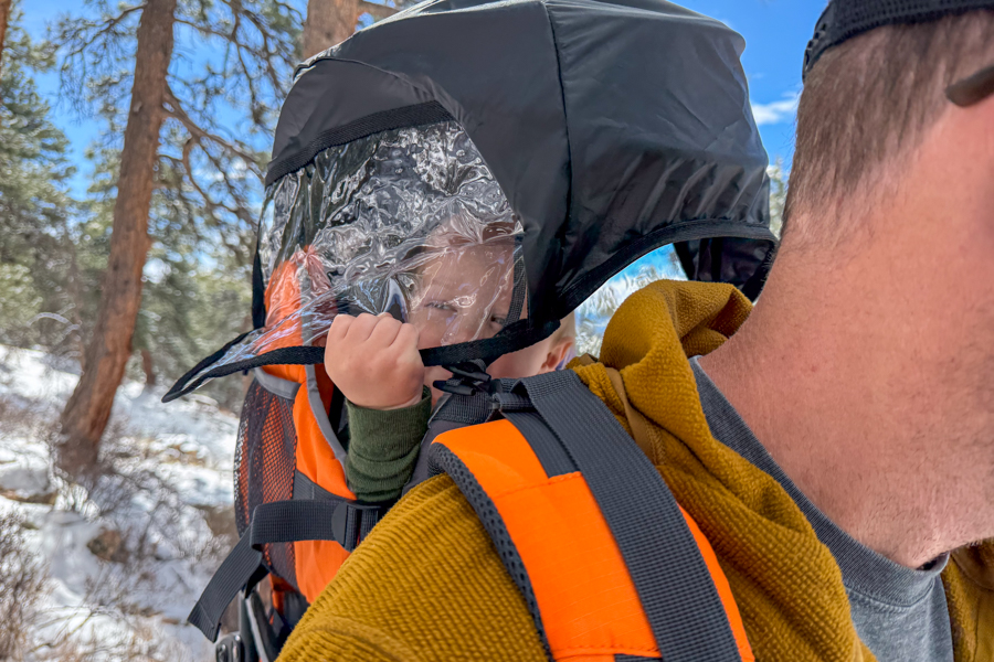 Close-up of a child riding in the Luvdbaby Premium under the deployed rain cover, with the clear plastic front panel pulled down around the seat.