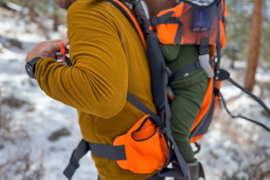 Side view of the Luvdbaby Premium in use on trail, showing the child seated in the carrier, the hipbelt pocket, and the overall carry profile.