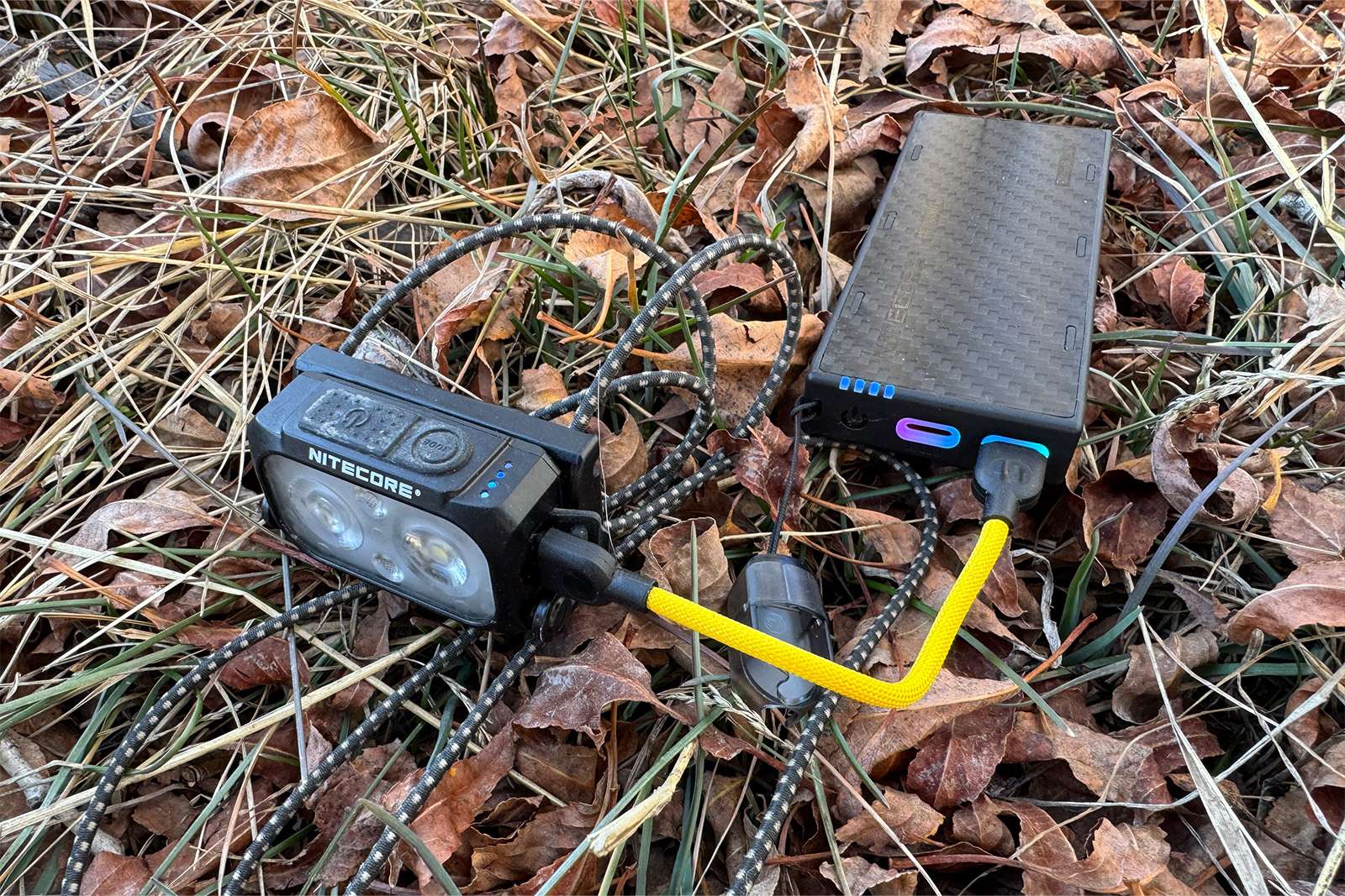 Se conecta un faro al NB10000 con un cable muy corto. Están sentados sobre unas hojas en el suelo.