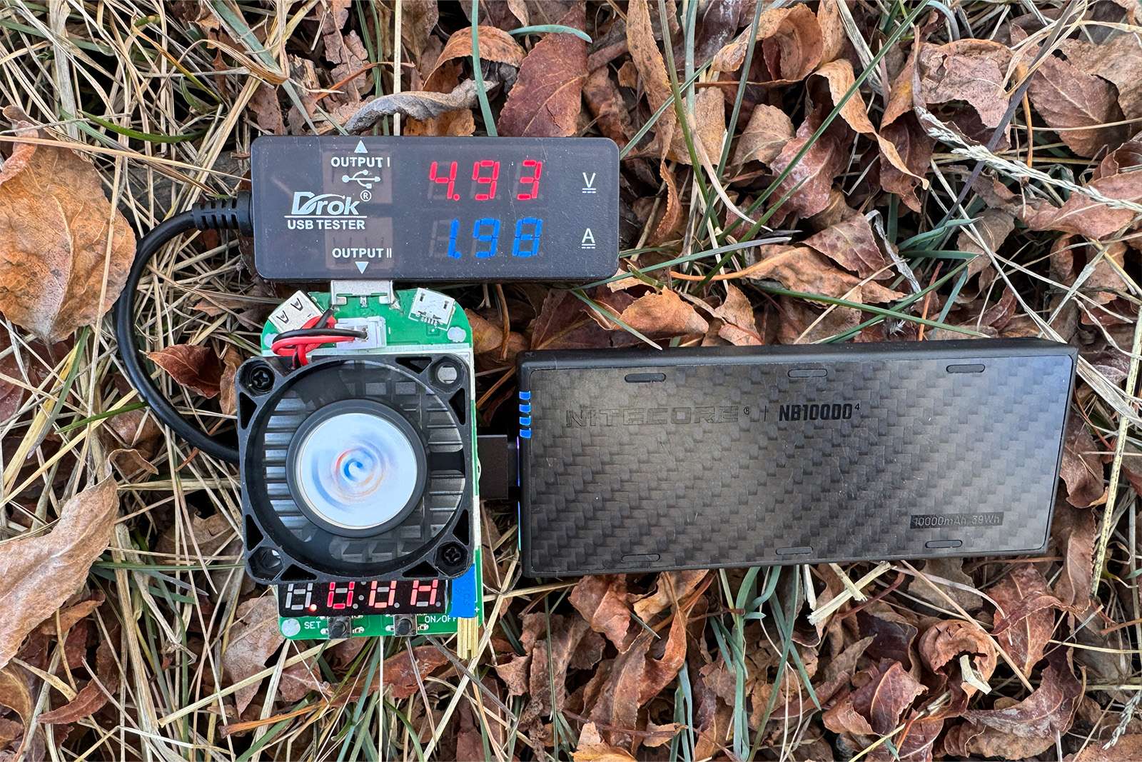 El NB10000 está colocado sobre unas hojas en el suelo con un multímetro y una resistencia de carga ficticia enchufados.