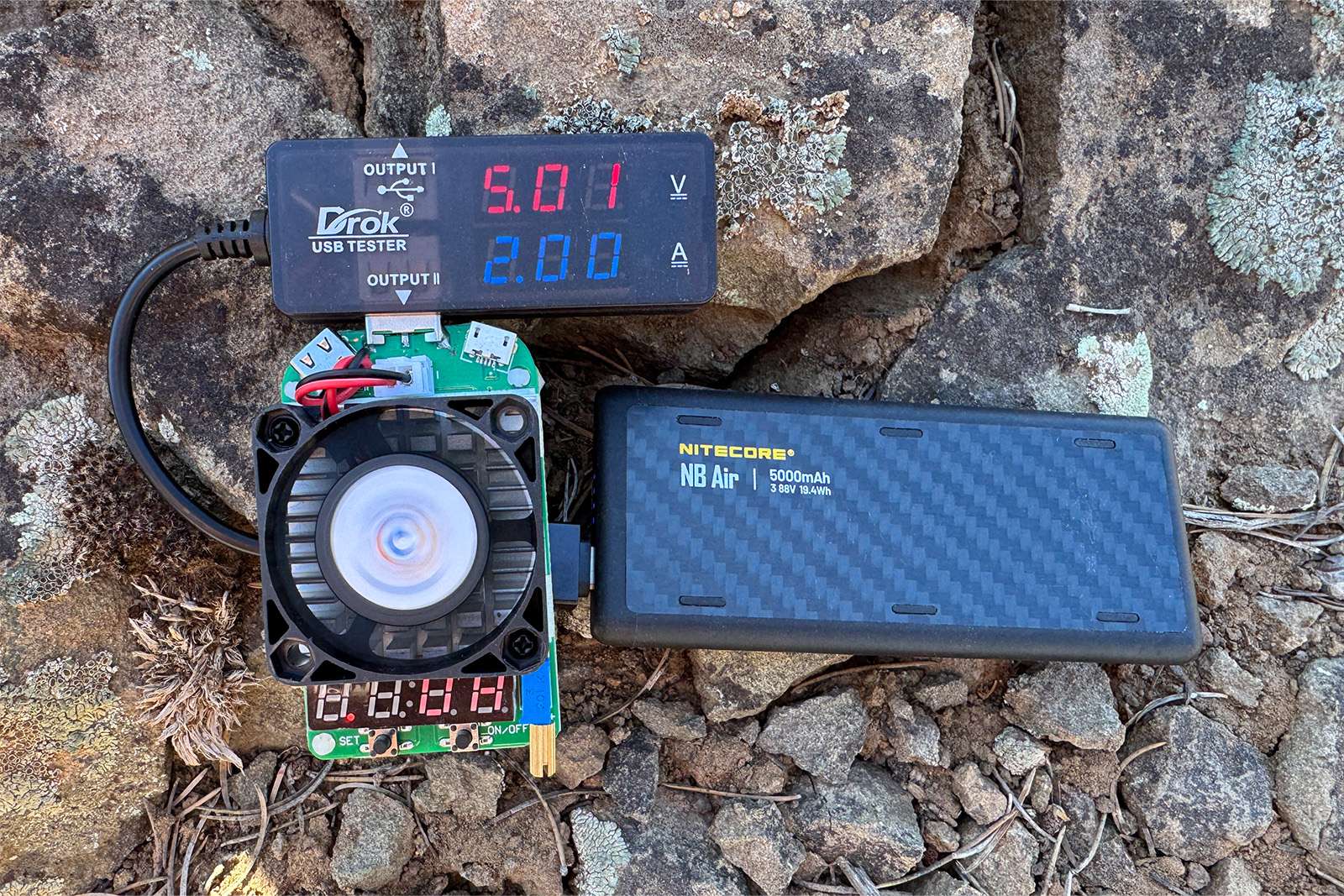 A close up of the NB Air sitting on some rocks plugged into a multi-meter and dummy load resistor.