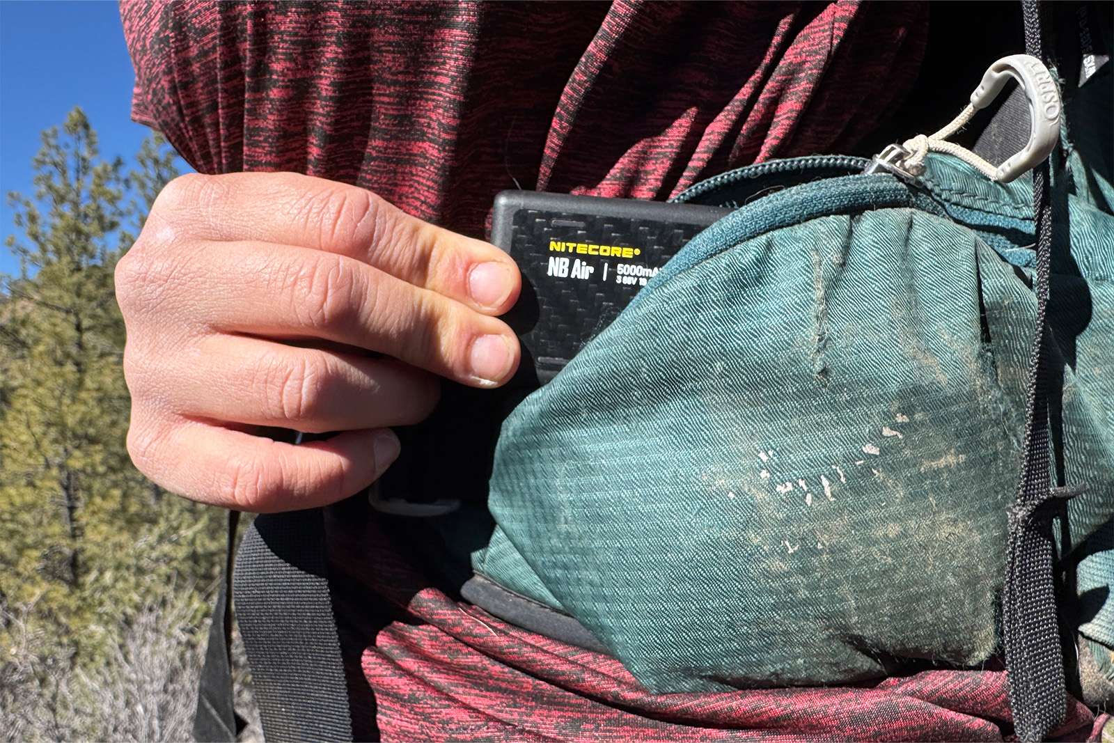 A closeup showing a hand pulling the NB Air out of a hipbelt pocket on an Osprey backpack.