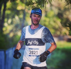A man running a half marathon holding a water bottle and phone wearing running gear