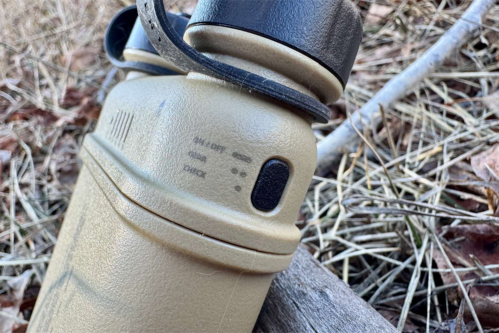 A close up of the power button on the Nestout power bank. There are instructions for how long to press the button for different functions and the power bank is sitting on some pine needles on the ground.