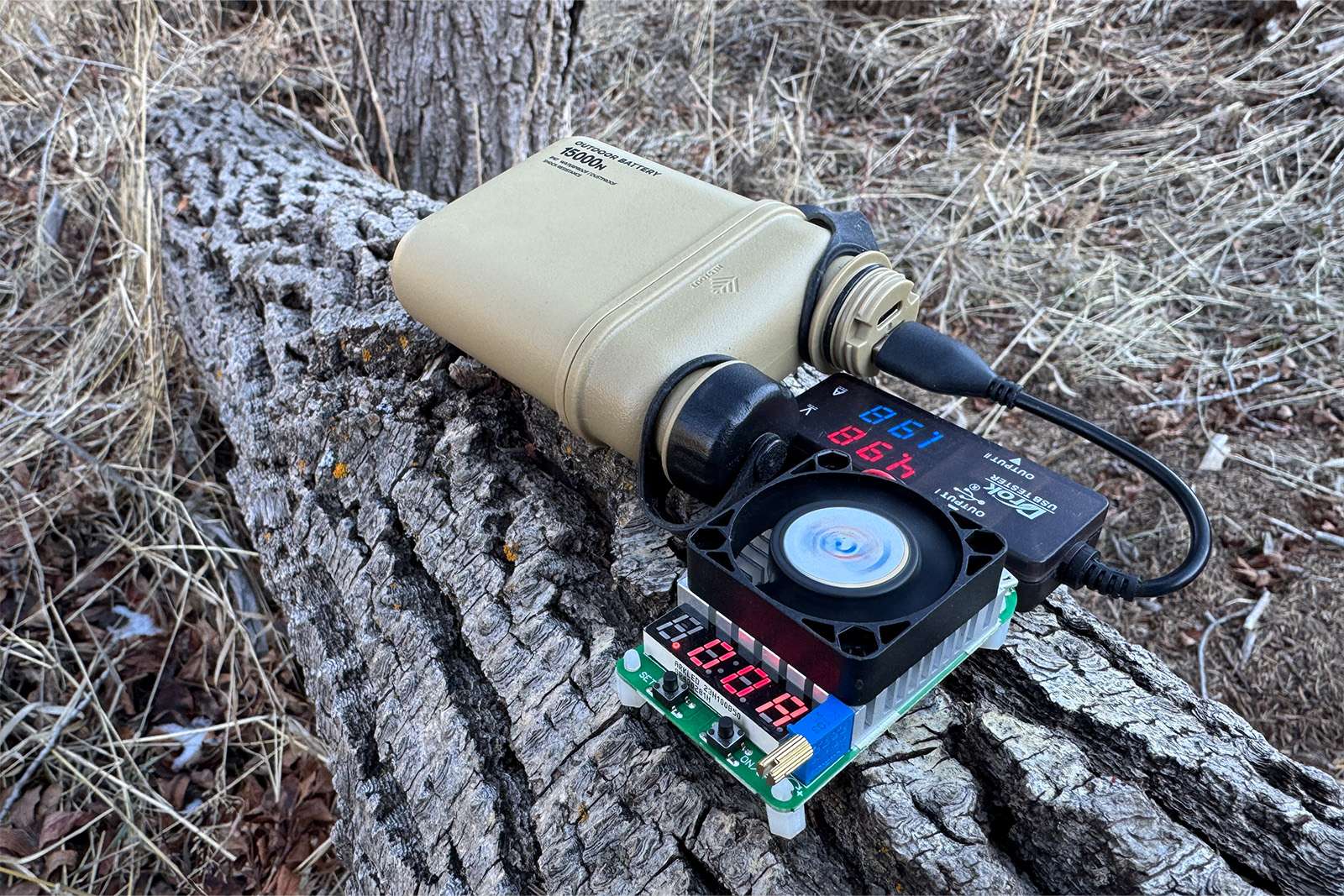 The Nestout power bank is balanced on a log with the multi-meter and dummy load resistor plugged into it.