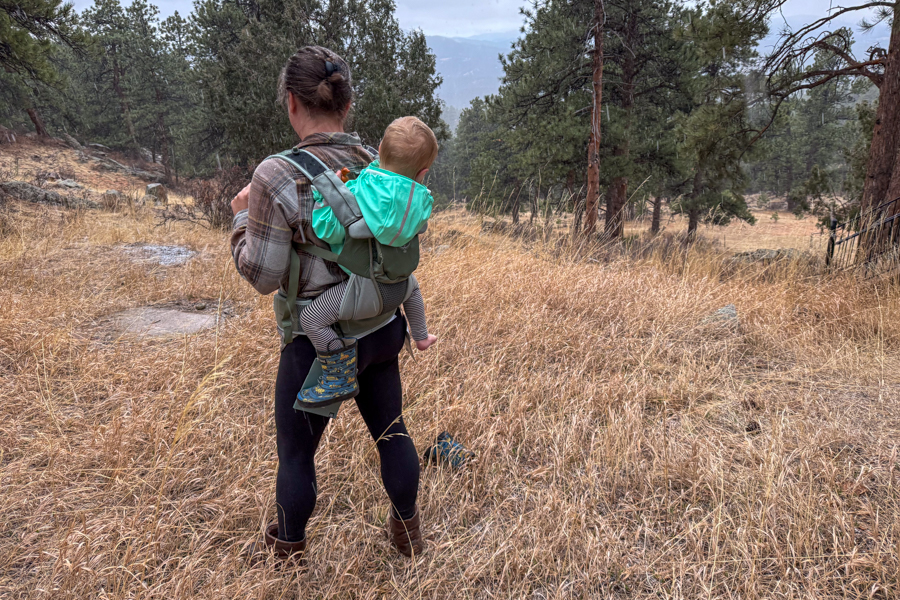 Tester wearing the Osprey Poco Soft Child Carrier in back-carry mode while standing on a grassy trail with a child seated comfortably in the carrier.