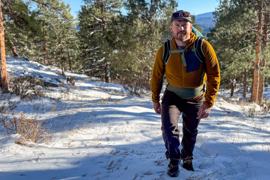 Tester hiking uphill in snowy pine forest terrain while wearing the Osprey Poco Soft Child Carrier in back-carry mode.