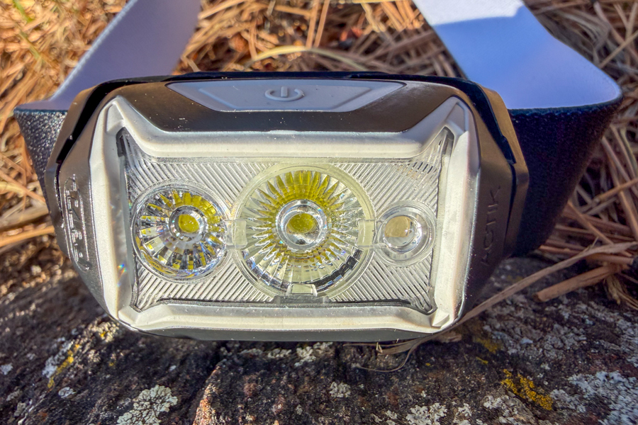 Close-up of a Petzl headlamp lens showing three LEDs inside the clear housing, resting on a rock.