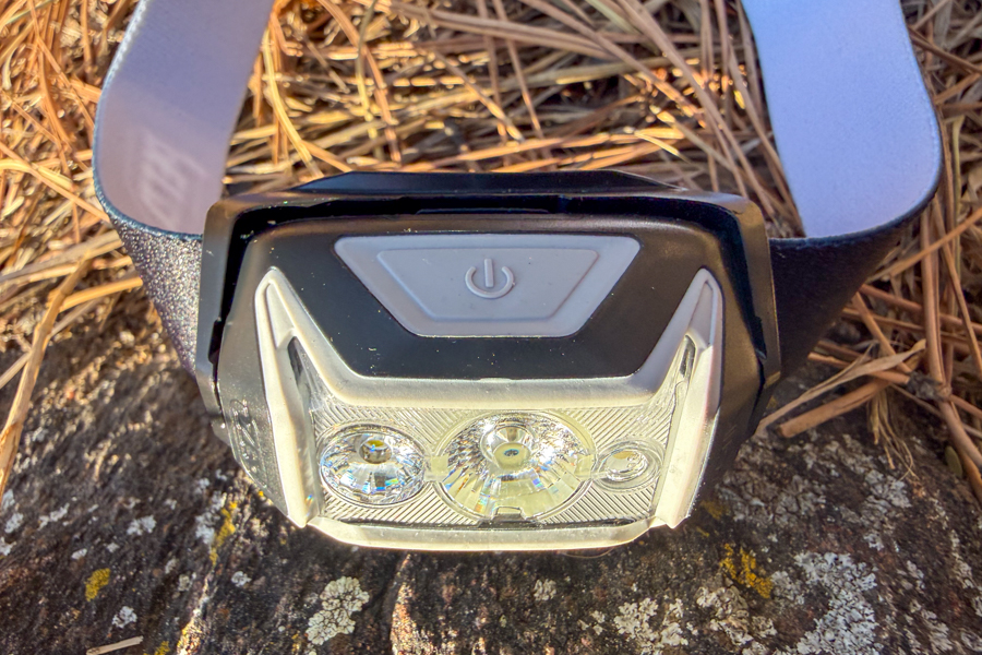 Front view of the Petzl headlamp with the top power button visible, sitting on a rock with the headband behind it.