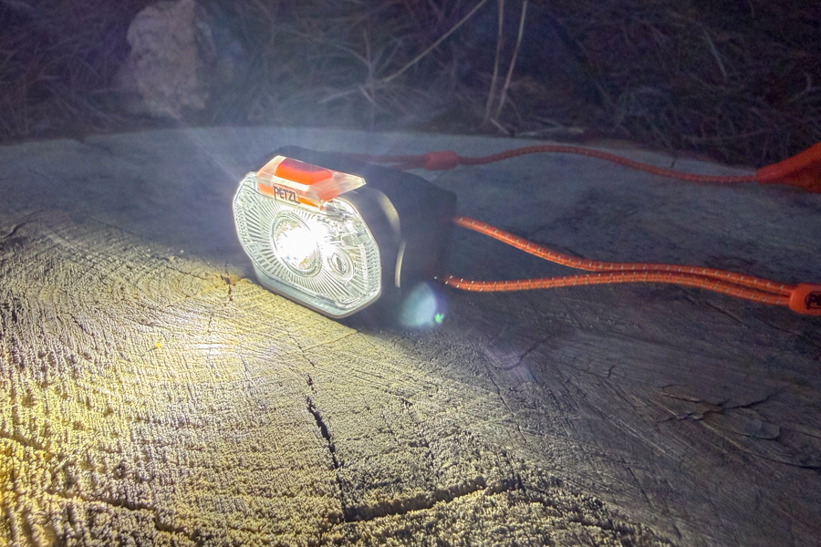 Close-up of the Petzl Swift headlamp on a log with the light turned on, illuminating the wood grain in low light.
