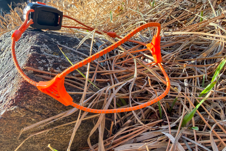 Orange cord-style Petzl headband laid out on a rock, showing the thin elastic band and adjustment hardware.