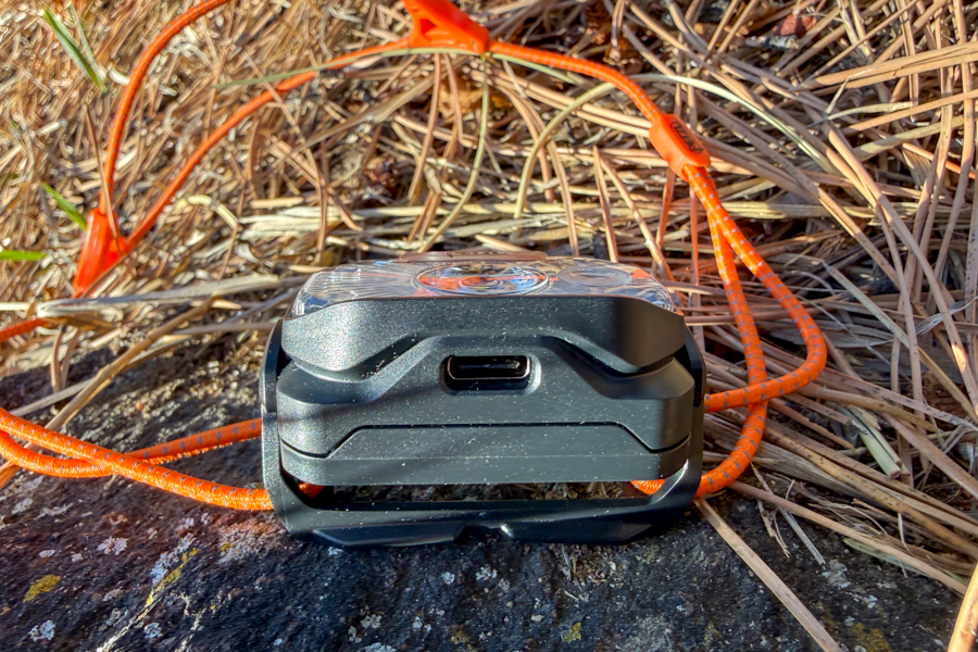 Side view of the Petzl Swift headlamp showing the USB-C charging port on the bottom of the housing with the cord headband behind it.