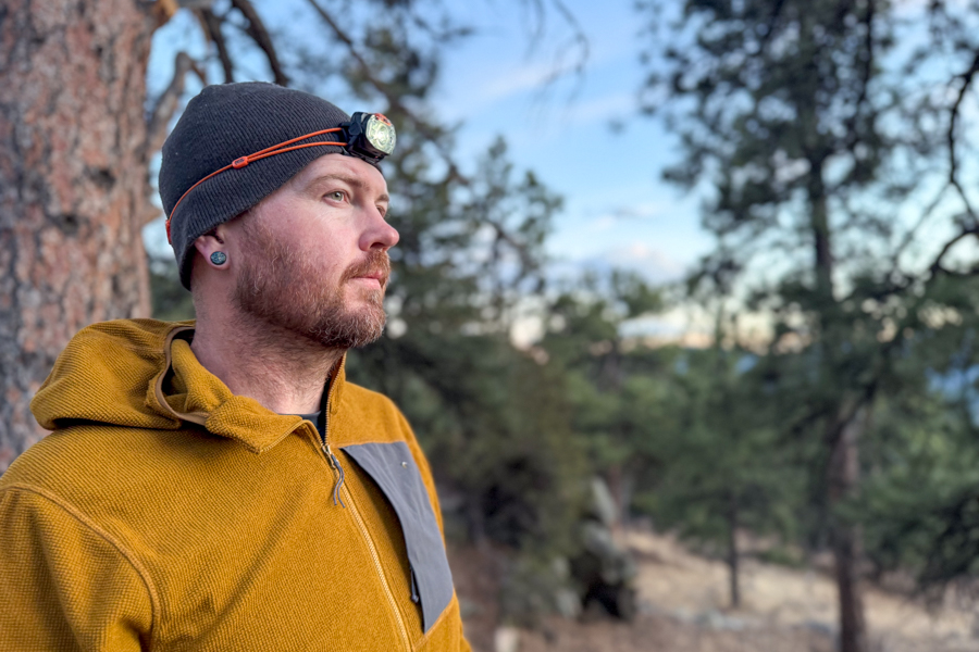 Person wearing the Petzl Swift headlamp over a beanie at dusk in a pine forest.