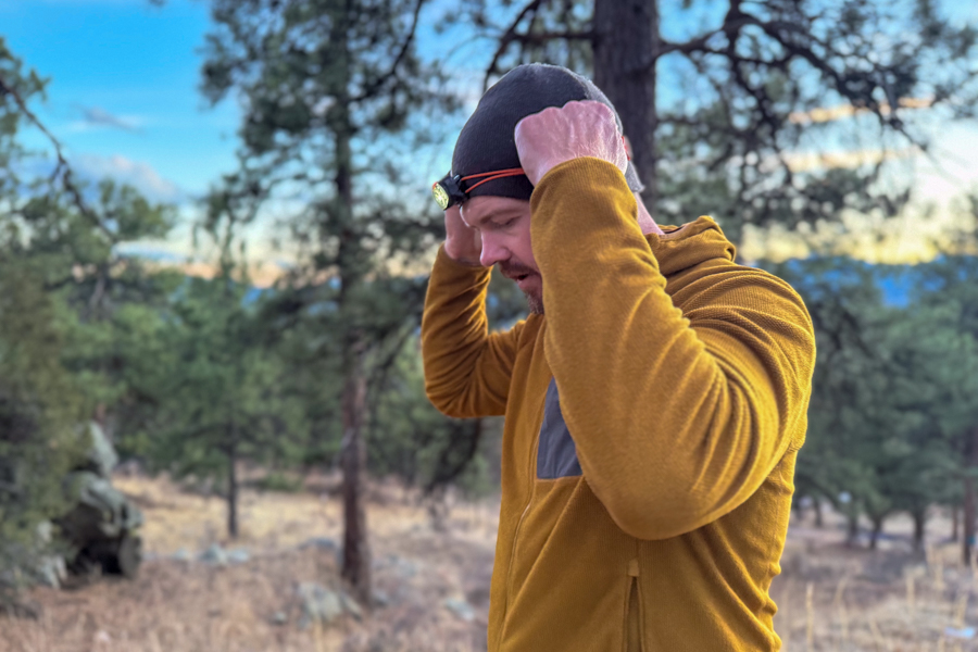 Person adjusting the Petzl Swift headlamp strap on a beanie at dusk with trees in the background.