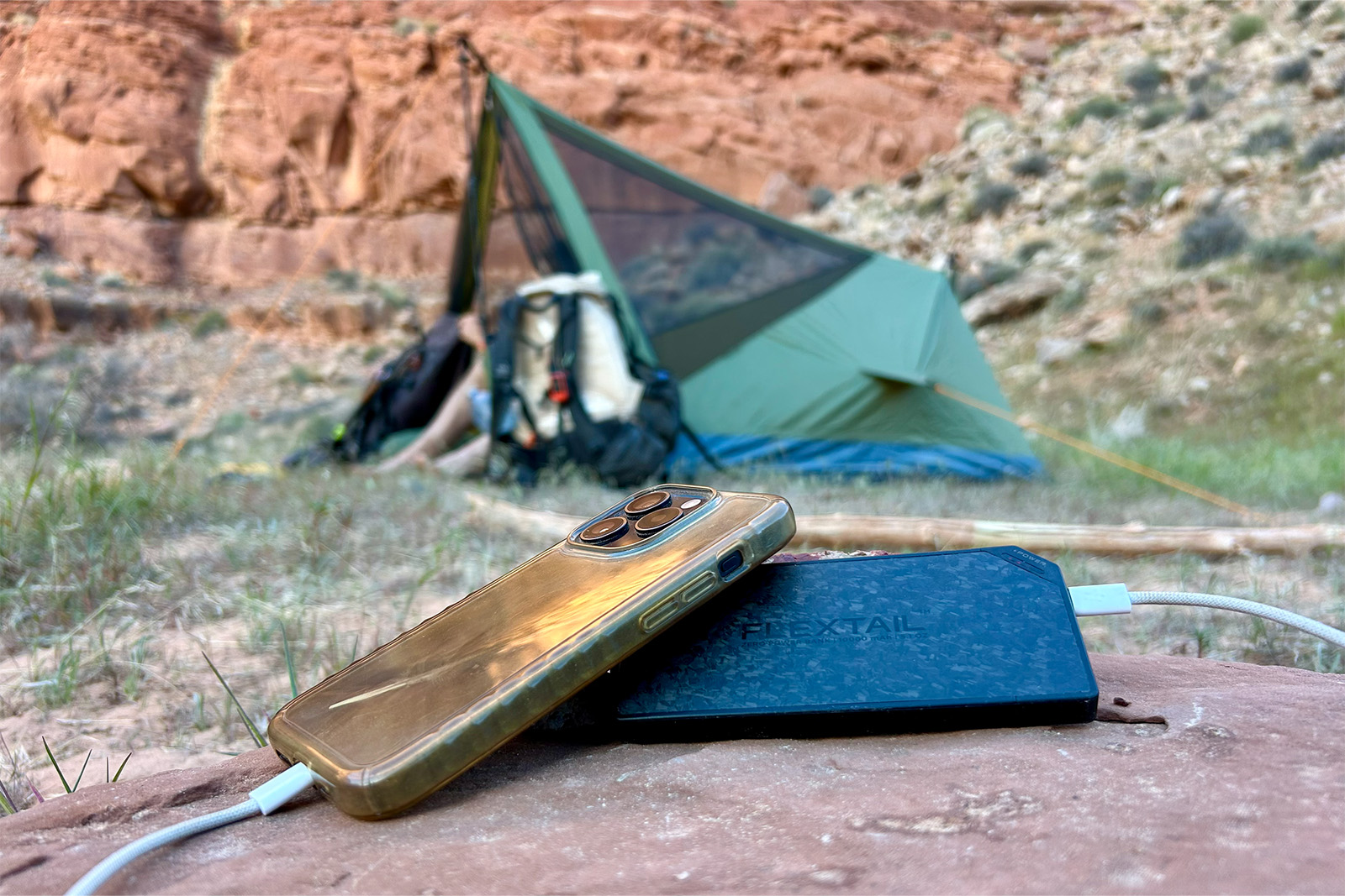 Closeup of the Flextail charging an iPhone. They are sitting on a rock and there is a tent in the background.