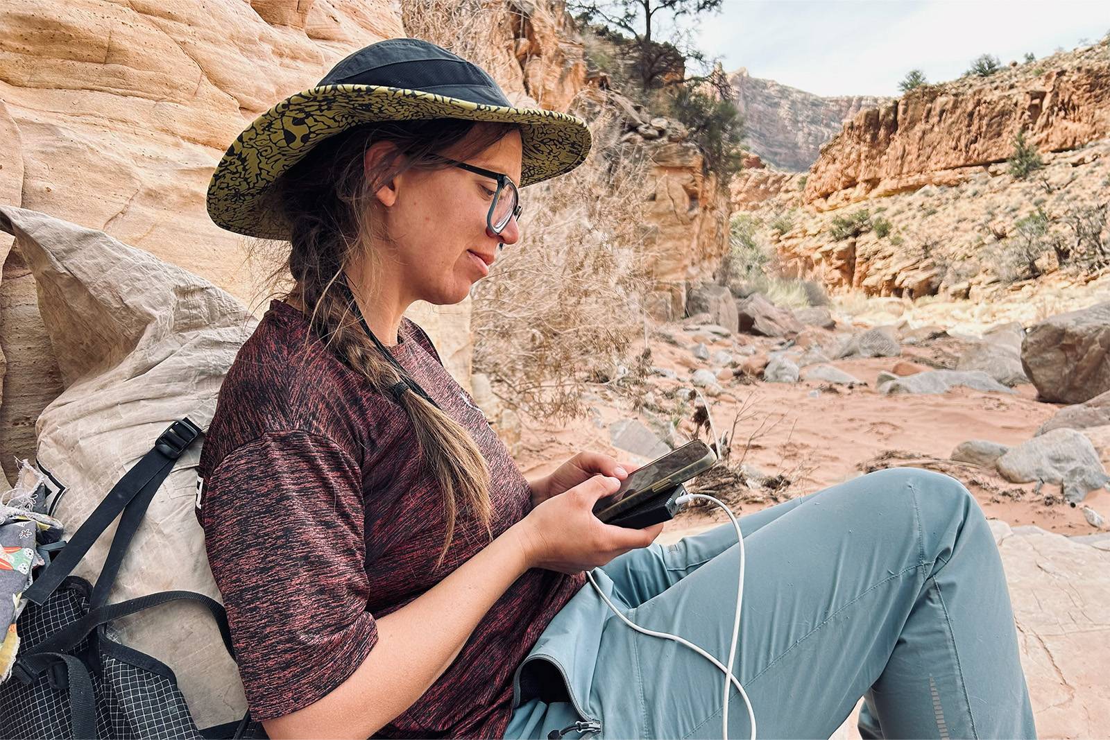 Una mujer sosteniendo un teléfono y el NB10000 Gen4. El teléfono se está cargando desde Gen4. Está apoyada en una mochila con un cañón al fondo.