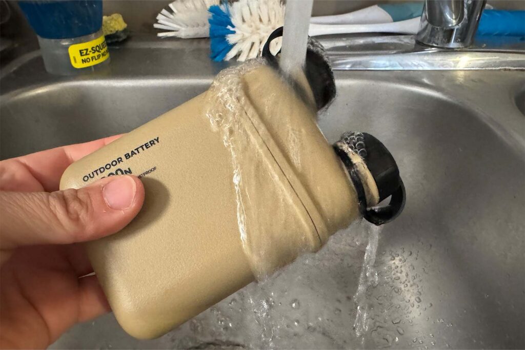 Close up of a hand holding the Nestout in a sink. There is water flowing over it from above.