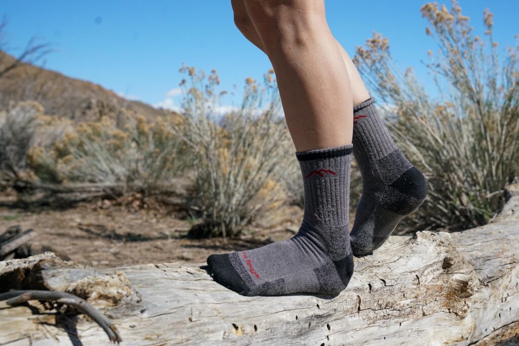 A close up image of a pair of feet wearing grey hiking socks standing on a log.