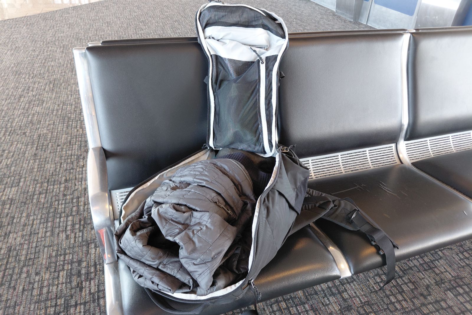 A backpack lies open on an airport waiting area seat.