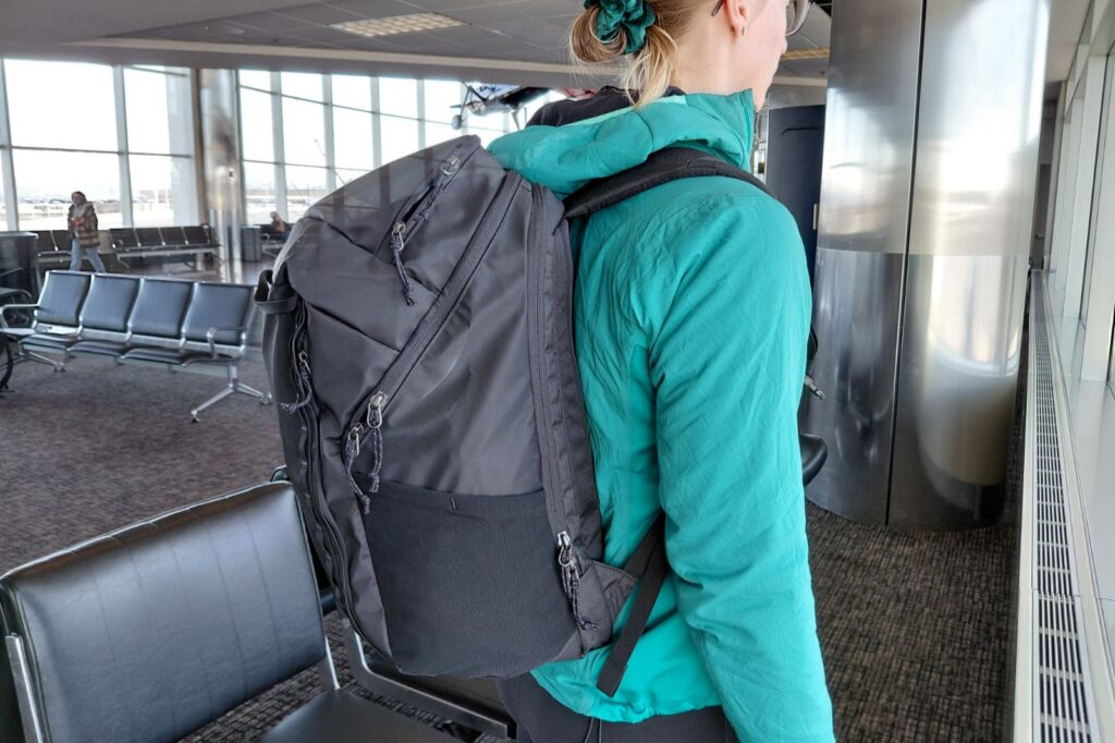 A woman wears a black backpack in an airport waiting area.