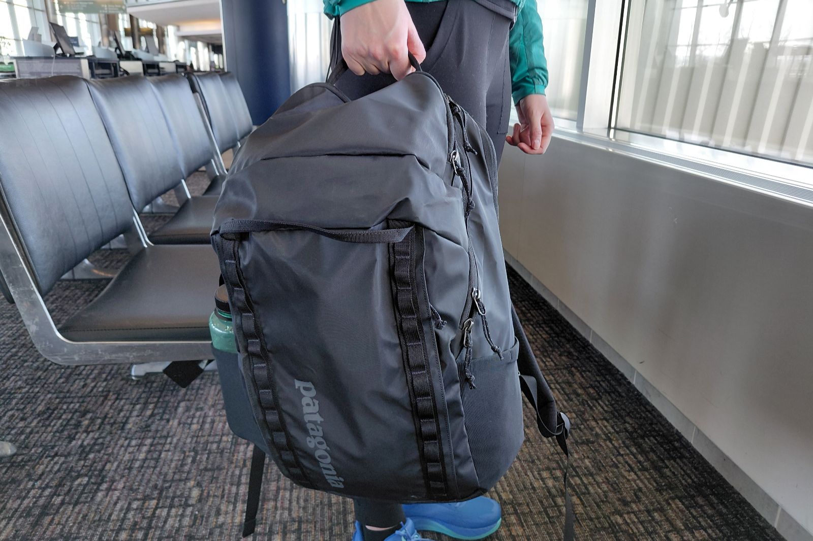 A close-up of a black backpack being held by the handles on the top of the pack.