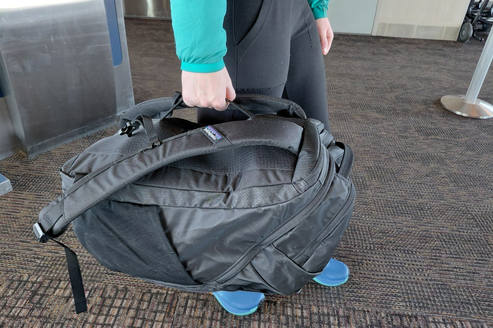 A woman carries a black backpack by an additional handle.