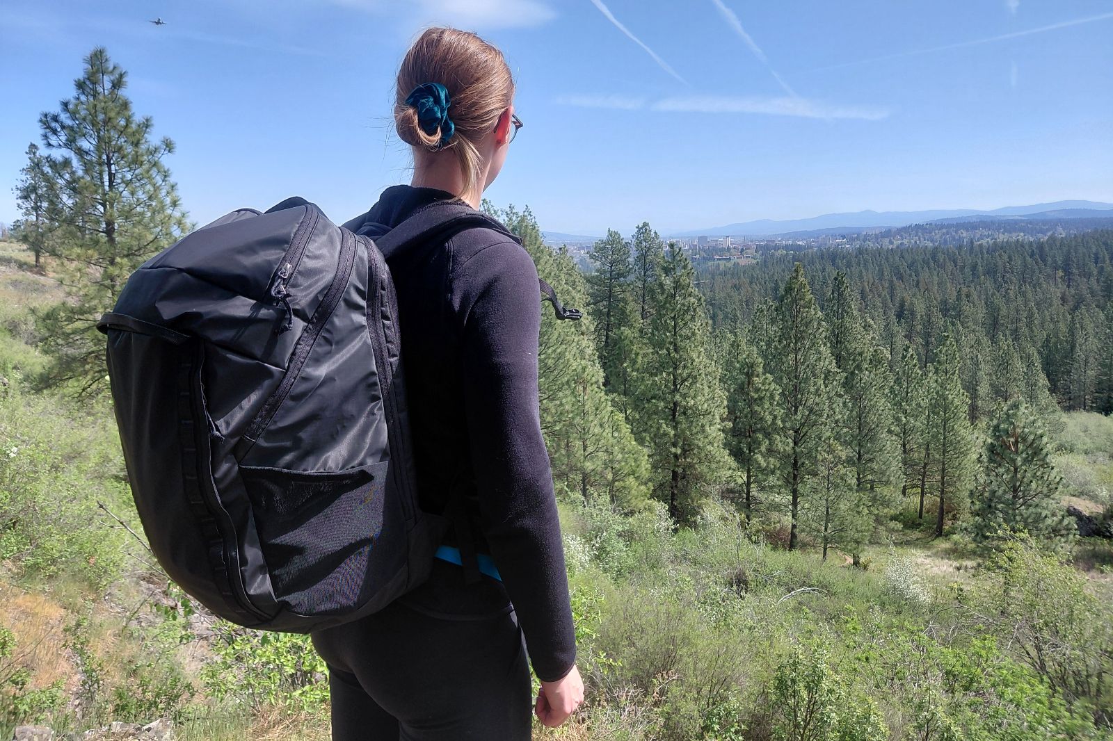A woman stands on an overlook wearing a black backpack.