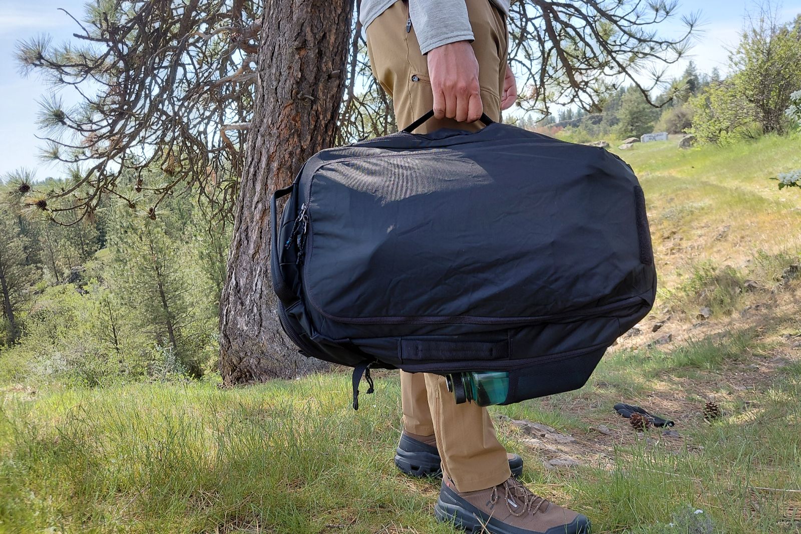 A man holds a backpack converted to a duffel by the side handle.