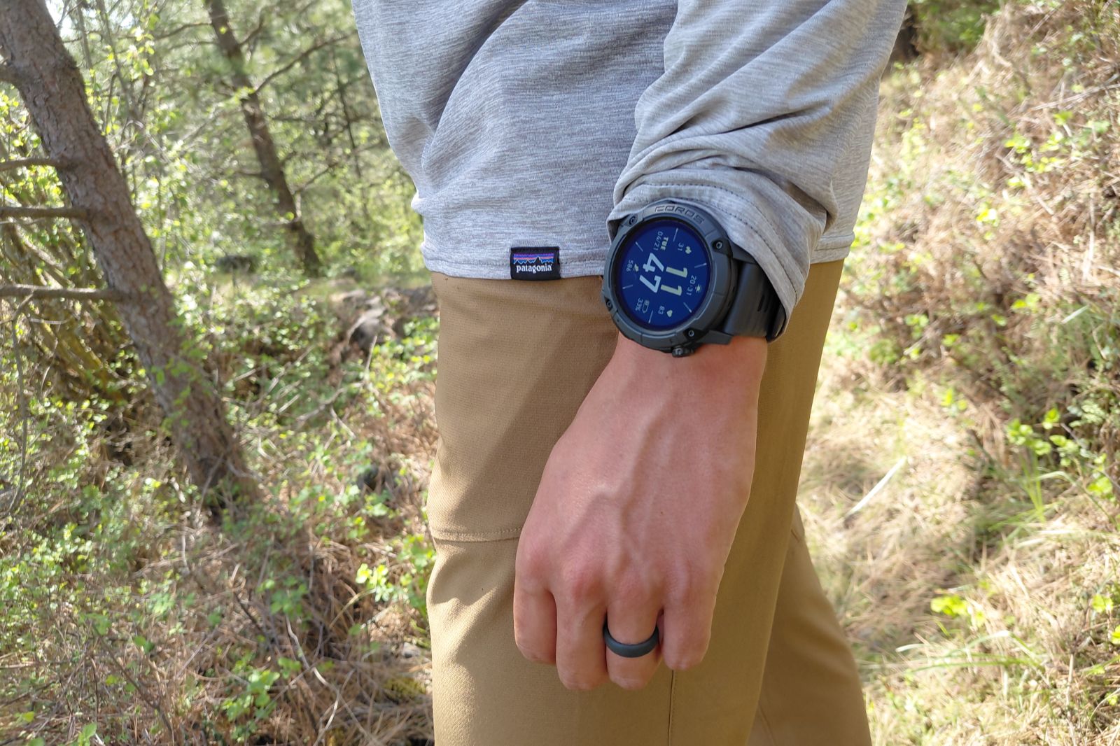 A close-up of a watch worn on a wrist by a man on a hiking trail.