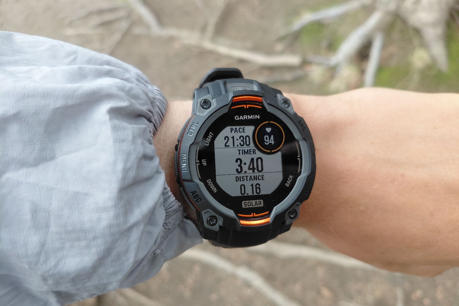 A person wearing a gray jacket views a black Garmin smartwatch displaying pace, timer, and distance.